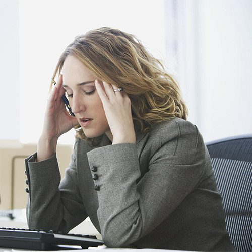 A woman sitting at a desk with her head in her hands.