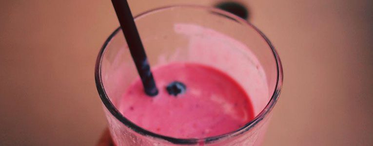 A glass of pink smoothie with a straw.