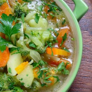 A bowl of soup with broccoli, carrots and other vegetables.