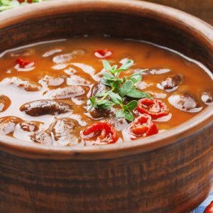 A bowl of soup with mushrooms and peppers.