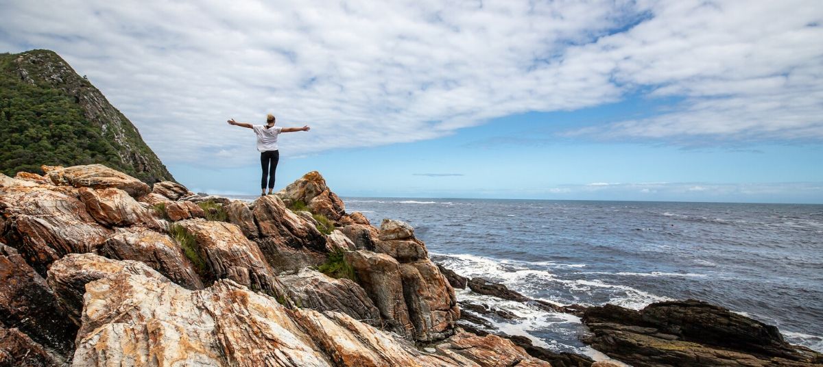 A person standing on top of rocks near the ocean.