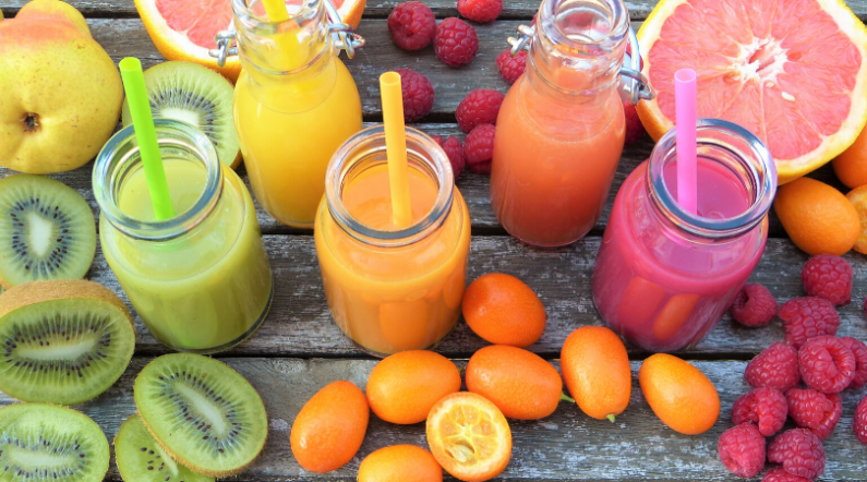 Colorful fruits surrounding glasses filled with smoothies for detox.