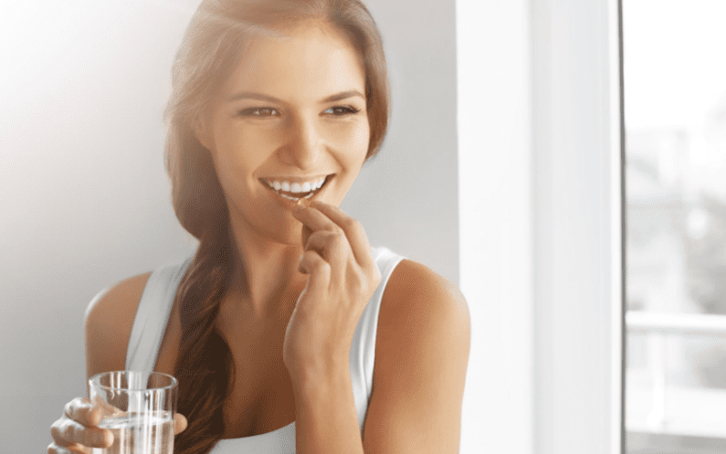 woman holding a glass of water and taking a supplement pill