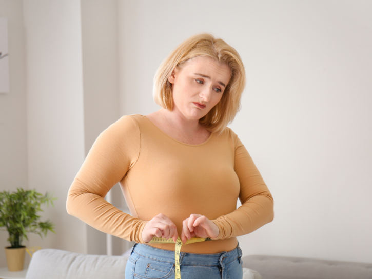 stressed woman with weight gain shown on tape measure
