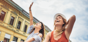 Two women are laughing and waving at the sky.