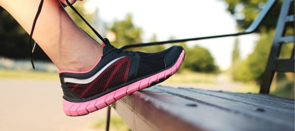 A person wearing black and pink shoes on top of a bench.