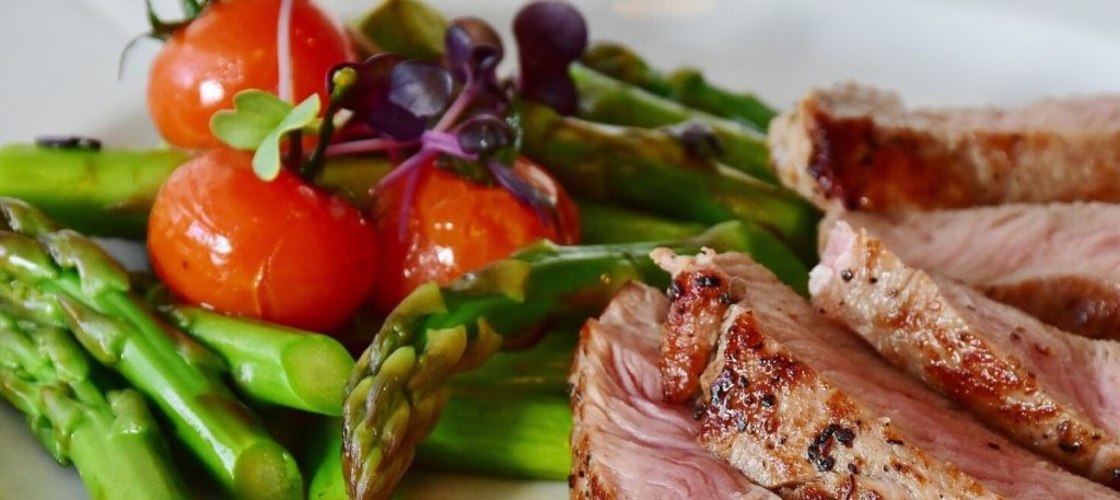 A plate of food with asparagus, tomatoes and meat.