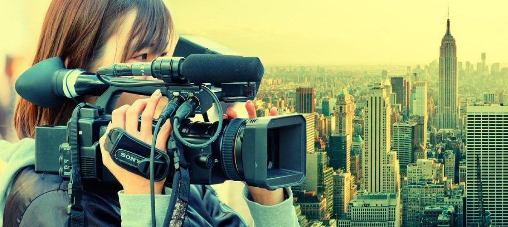 A person holding a video camera in front of a city.