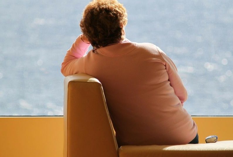 A woman sitting in an orange chair looking out the window.