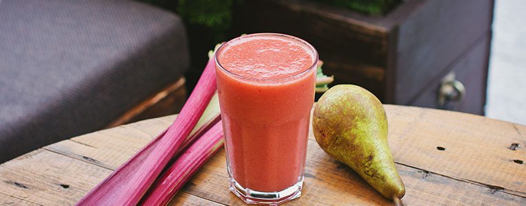 A glass of juice with some fruit on the side