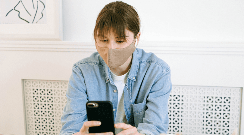 A woman wearing a face mask looking at her phone.