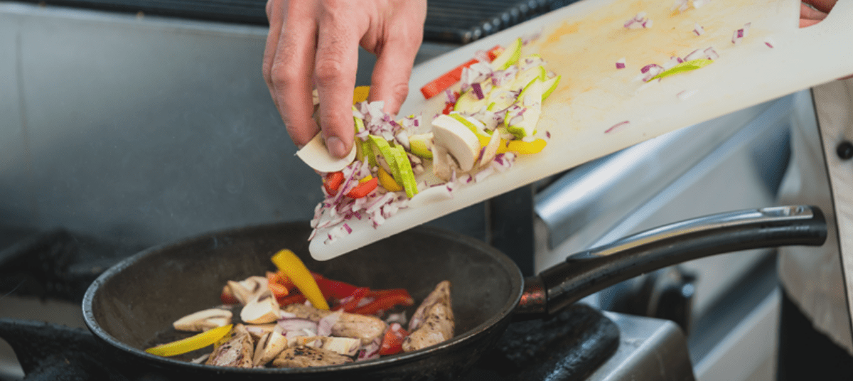 A person is cutting vegetables on a pan.