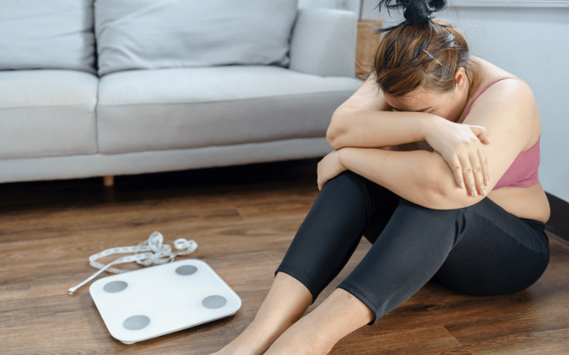 A woman sitting on the floor next to an electronic scale.