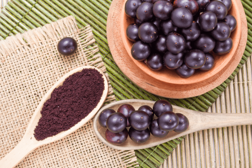 A wooden spoon filled with black grapes next to other spoons.