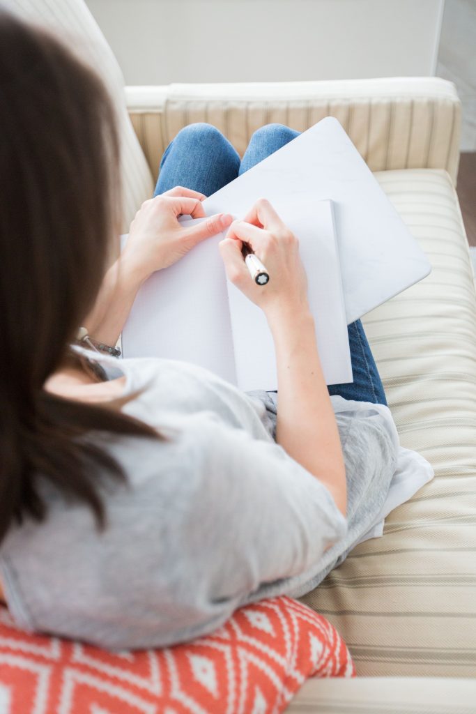 A woman sitting on the couch writing in her notebook.