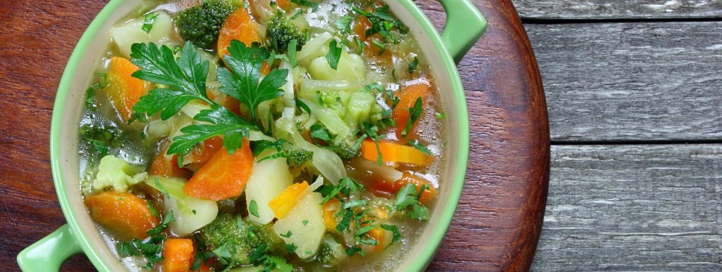 A bowl of soup with broccoli, carrots and other vegetables.