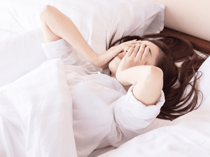 A woman laying in bed with her hands over her face.