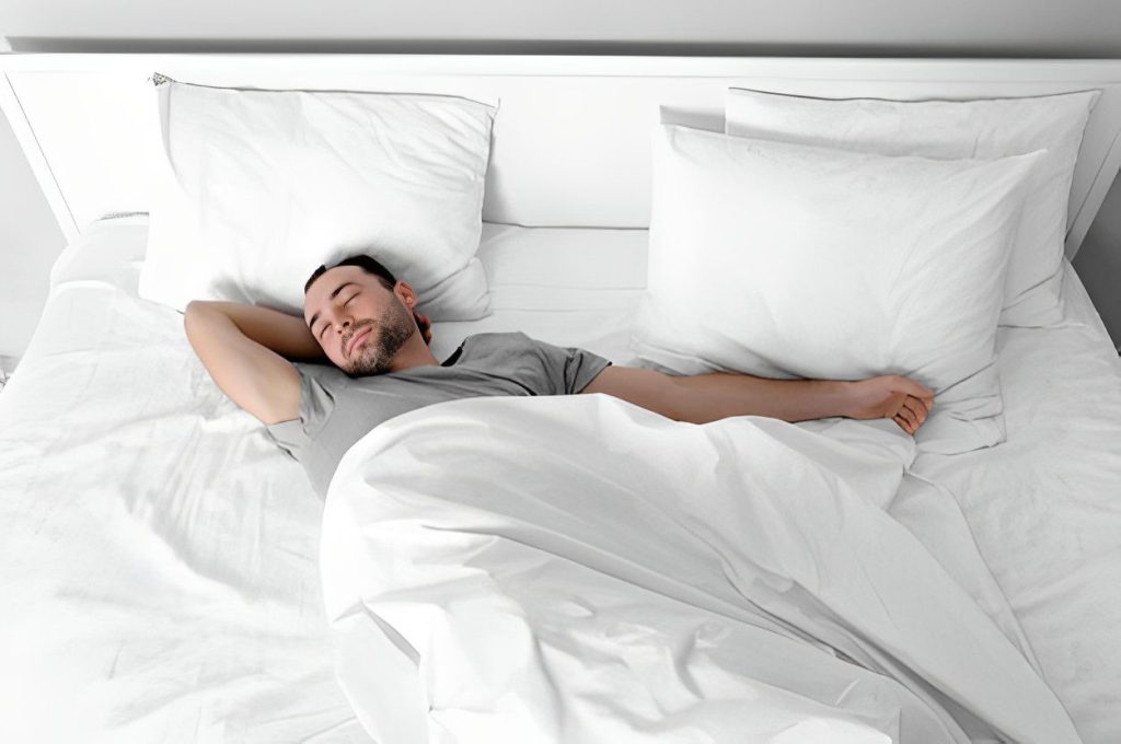 A man laying in bed with his head on pillows.