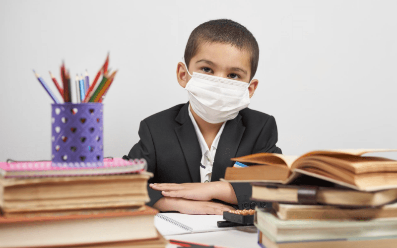 A boy wearing a mask sitting at his desk.