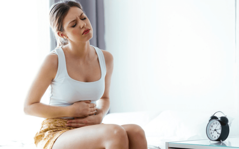 A woman sitting on the bed holding her stomach.