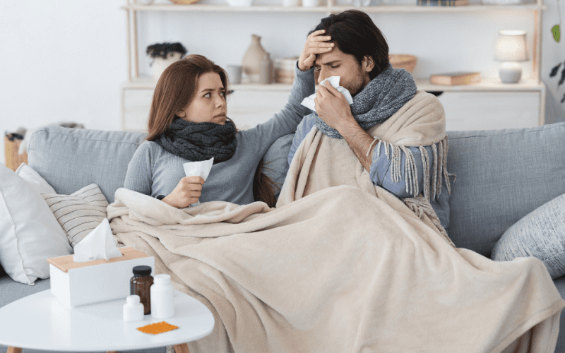 A man and woman sitting on the couch with blankets