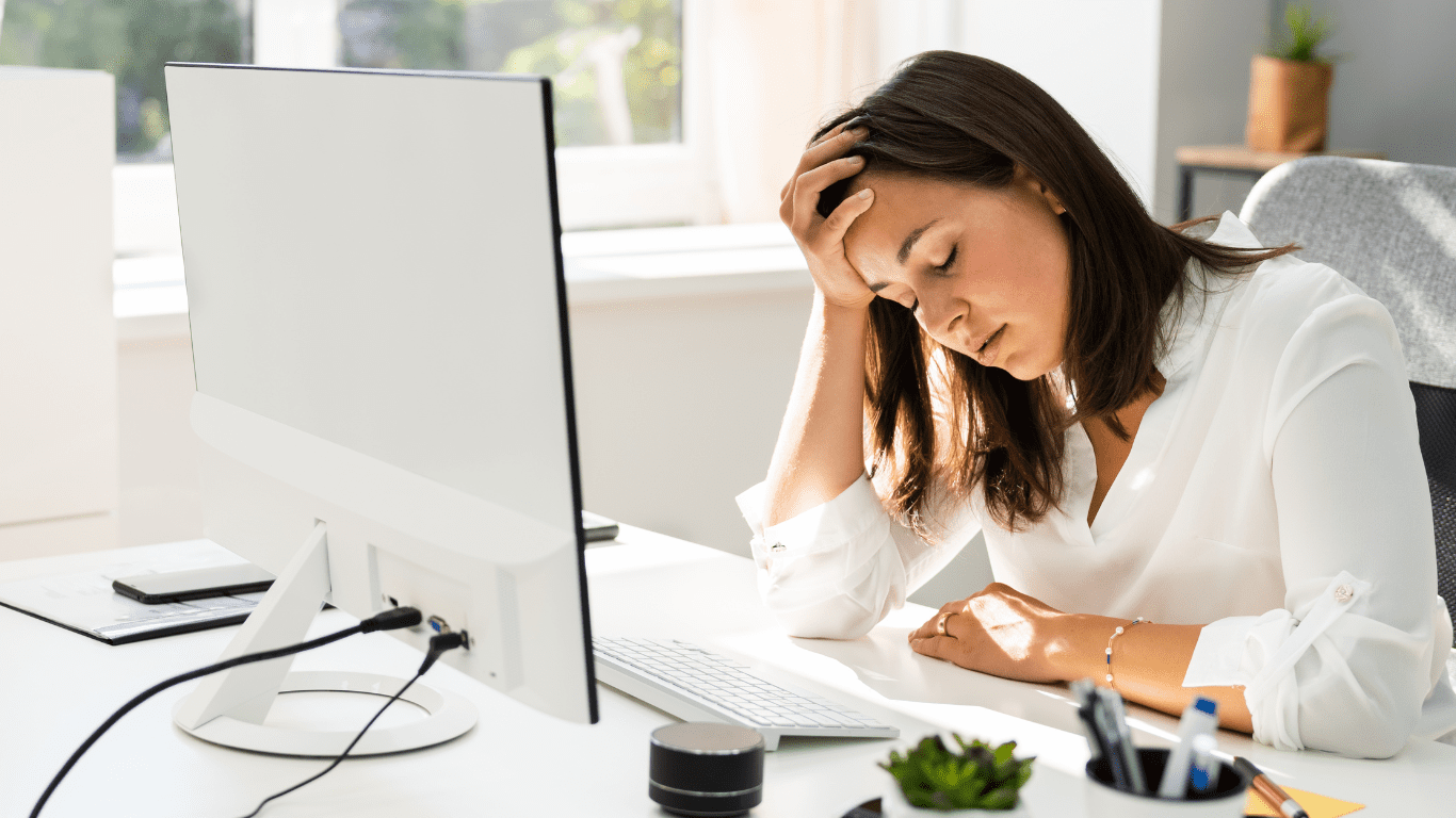 A woman sitting at her desk with her head in her hand.